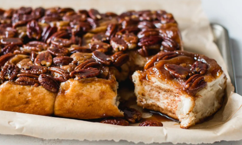 A tray of maple sticky buns, with one piece on the end cut and sitting off to the side.