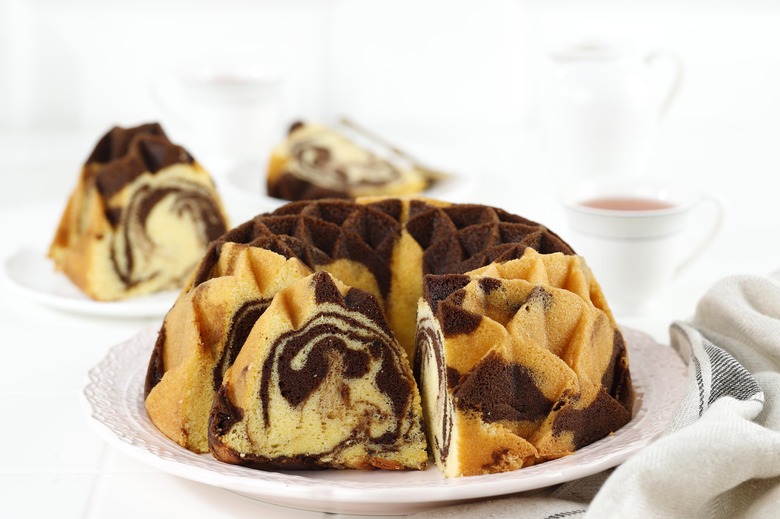 A marble bundt cake sitting on a table with two slices of cake on plates behind it.