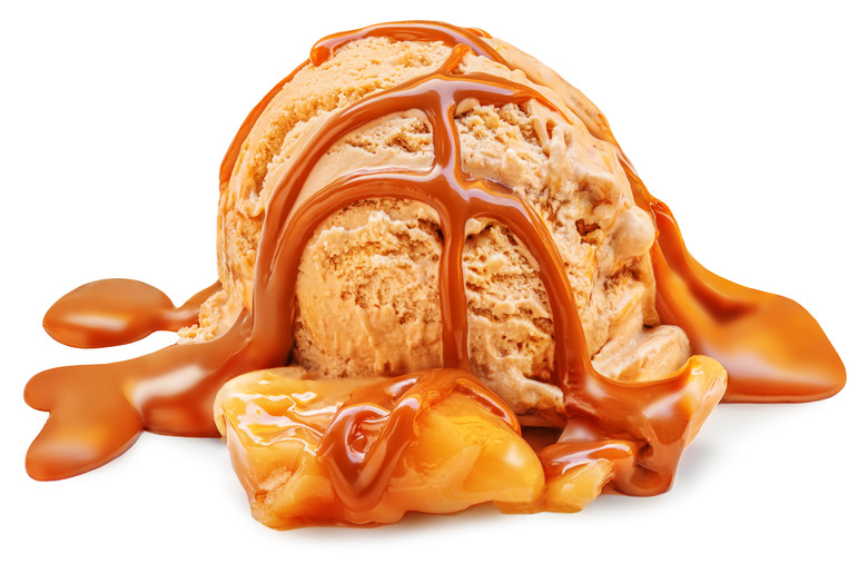 A scoop of caramel  ice cream drizzled with caramel syrup, with melting caramel pieces.