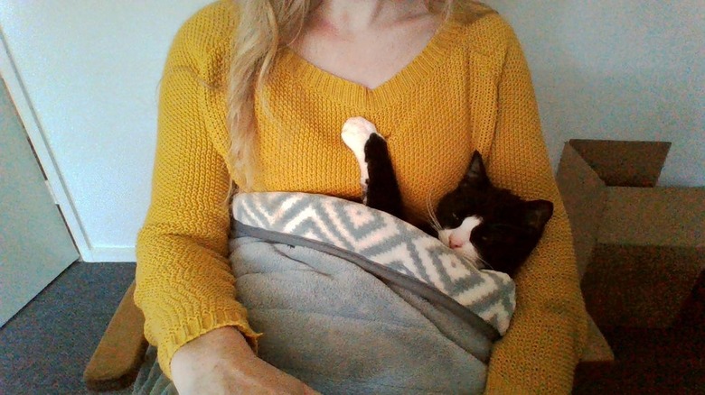 woman craddles cat in blanket