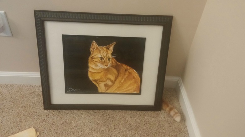 Cat sitting behind a painting of itself with just its tail visible