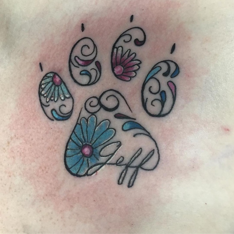 A tattoo of paw print with flowers and the name 