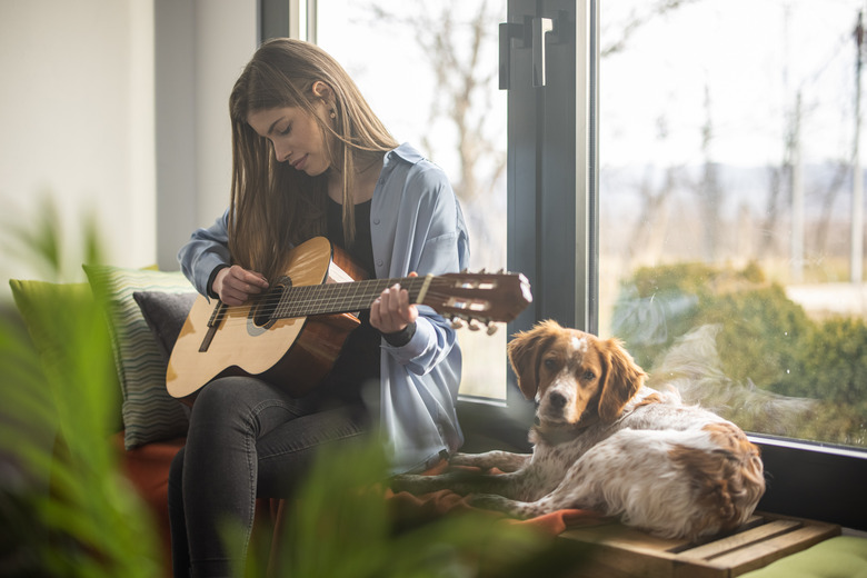 Woman playing guitar in living room while her dog lying next to her