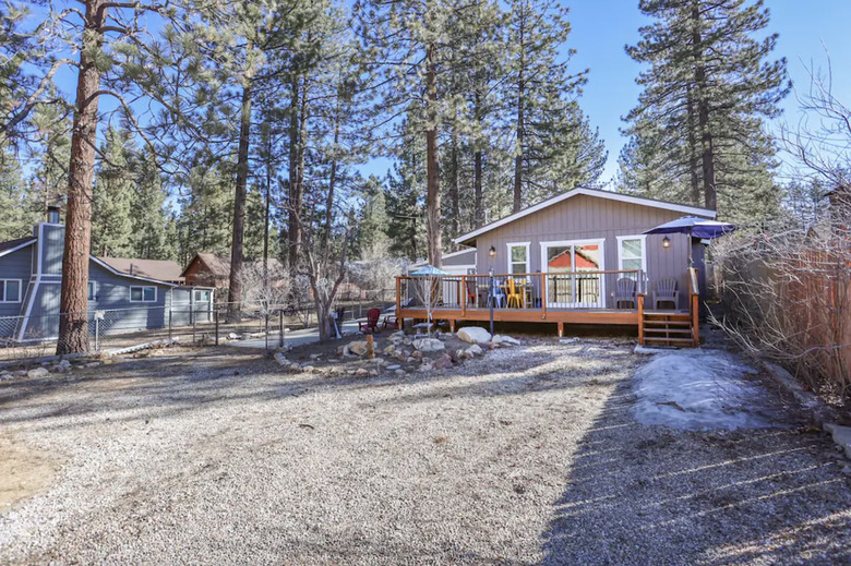 Cabin exterior showing large fenced-in yard and driveway. The house has a wrap-around deck with furniture on it.