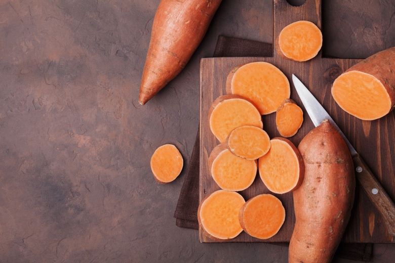 Camera pointing down at a cutting board with sweet potatoes, some of which are cut into rounds, and a knife.