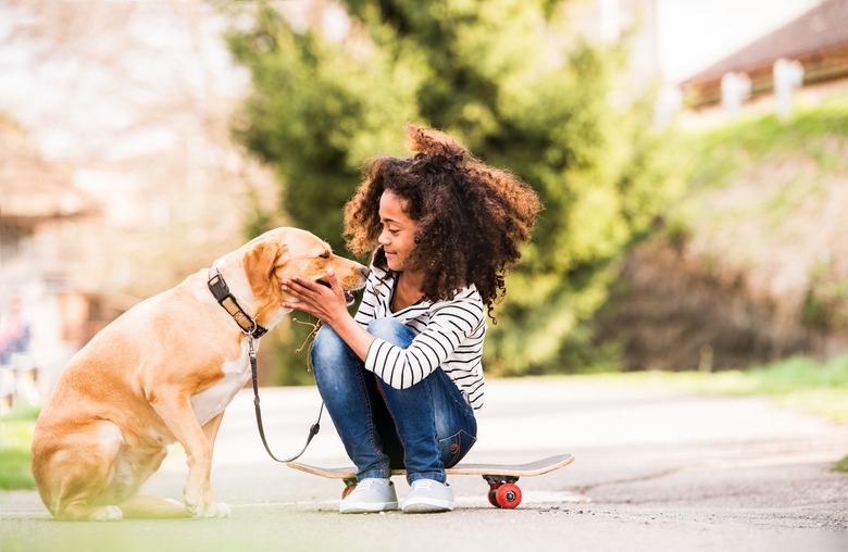 African American girl outdoors on skateboard with her dog.