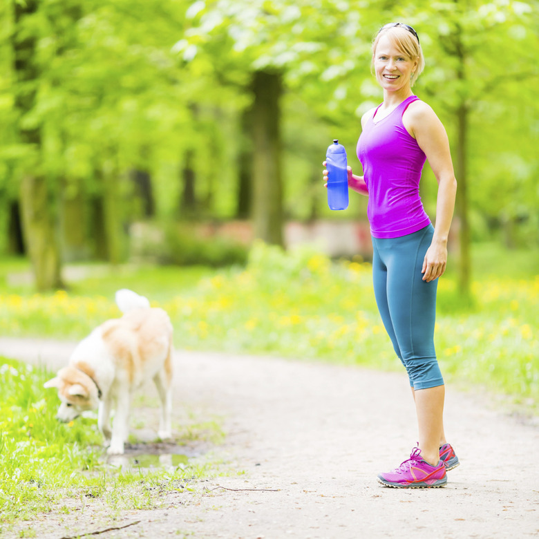 Woman runner walking with dog in summer park