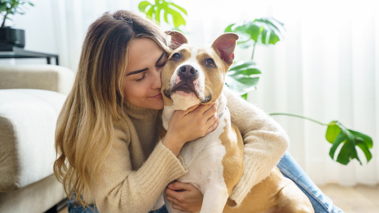 A woman sits next to a sofa hugging her dog