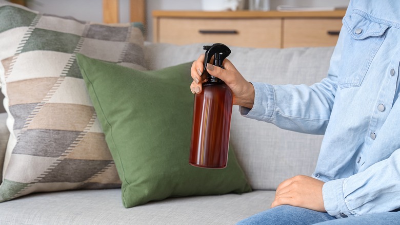 A woman holds a brown spray bottle while sitting on a sofa