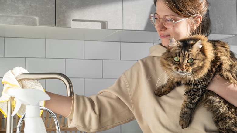 woman holds cat while cleaning kitchen