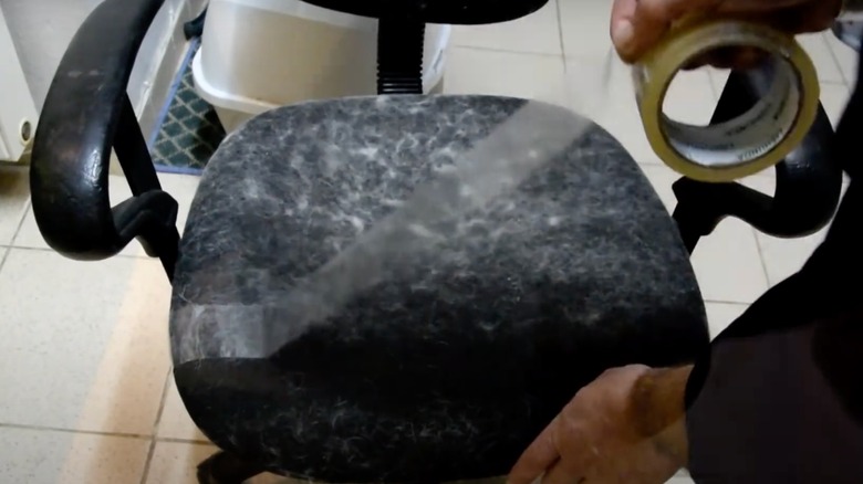 Person placing tape on a chair covered in fur to remove it