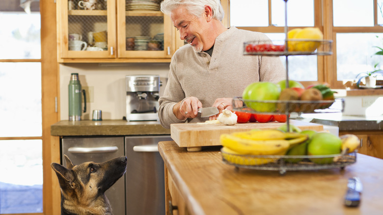 man chops garlic while dog watches