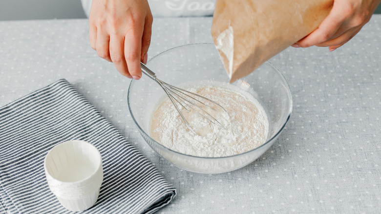 hands pouring white flour into bowl and whisking