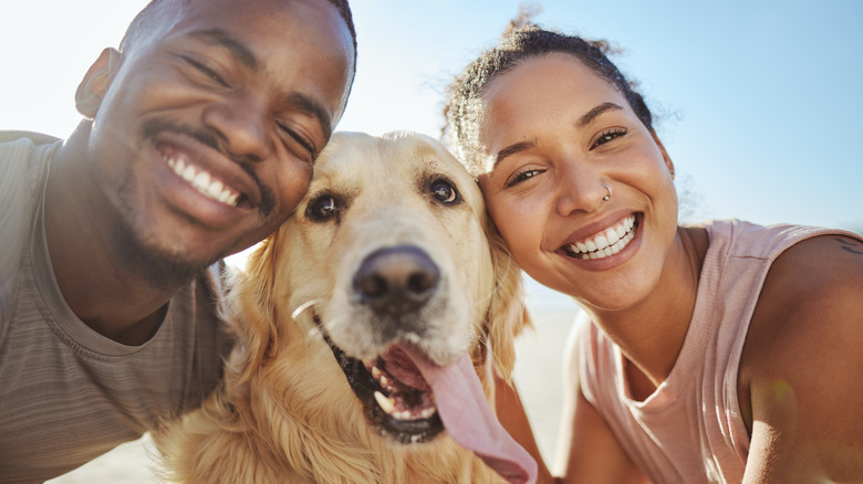 A couple takes a selfie with their golden retriever