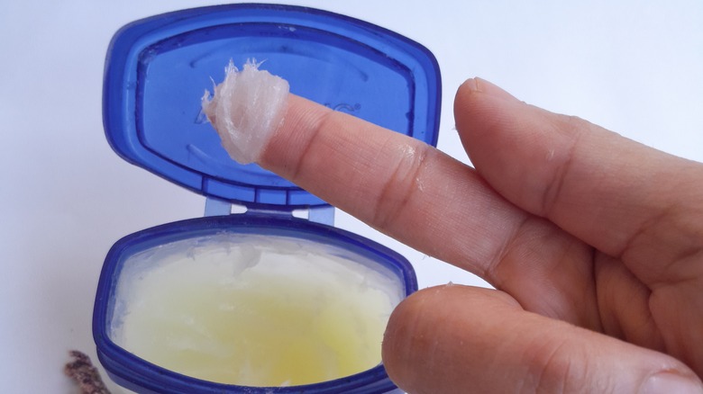 finger scoop of petroleum jelly with container in background