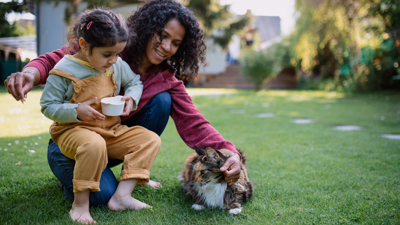 A mom and daughter petting their cat and feeding it