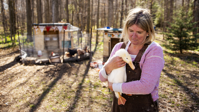 Woman holding duck outside of coop