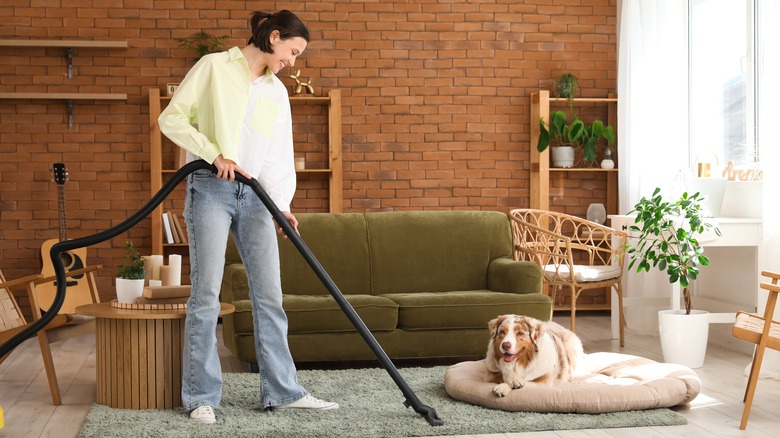 Woman vacuuming rug with dog on bed nearby