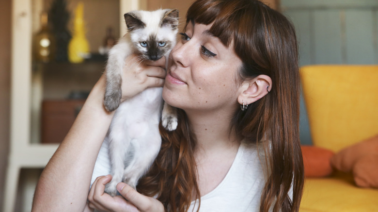 a woman holding a siamese kitten