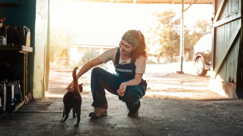 A woman kneels and pets a cat in her garage