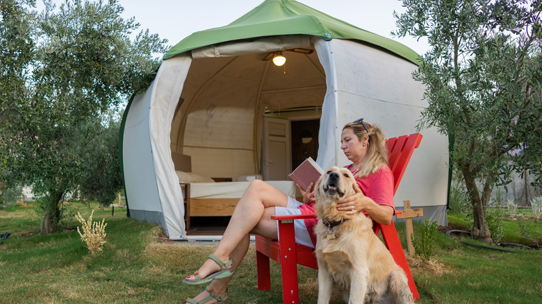 A woman reads with her golden retriever while in front of a tent