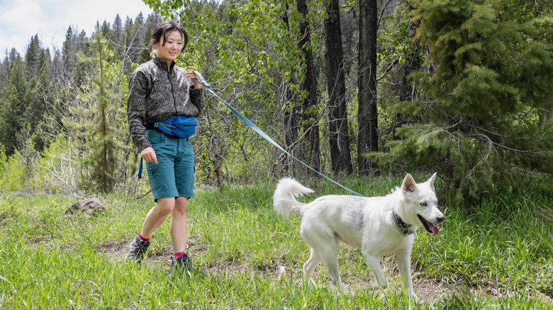 A woman walks her white shepherd on an outdoor trail