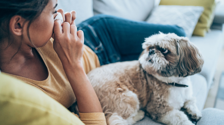 woman sitting with dog as she blows her nose