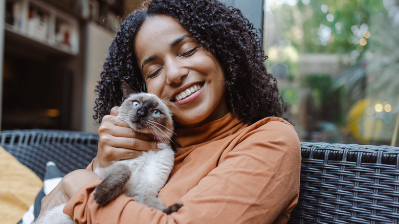 A woman sits on a couch and cuddles her cat