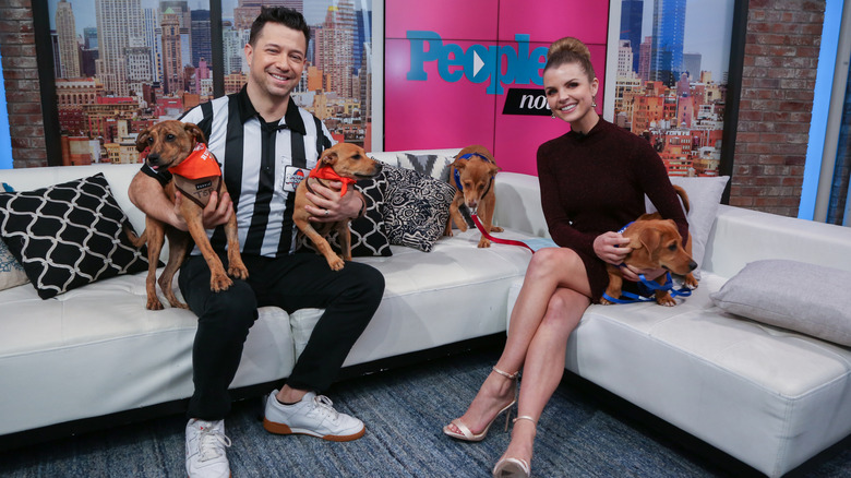 The Puppy Bowl referee holds puppies while being interviewed on a couch.