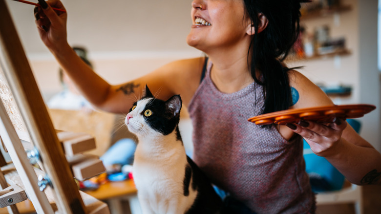 Woman painting with a cat in her lap