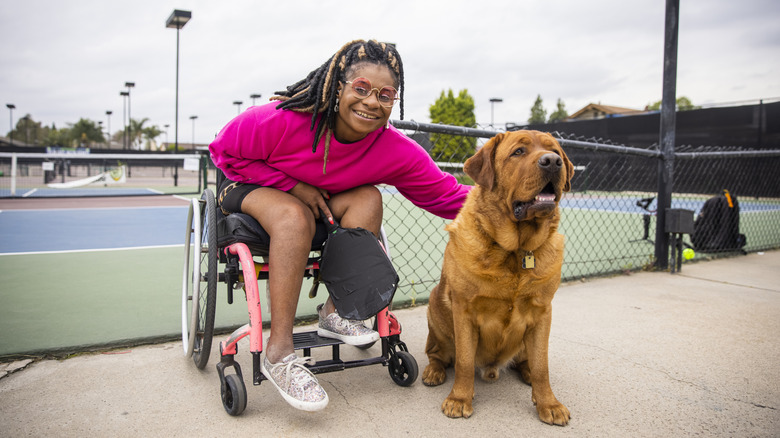 young woman in a wheelchair at pickleball court with dog