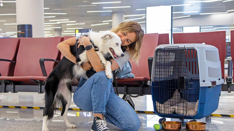 A woman hugs her dog next to their carrier in an airport