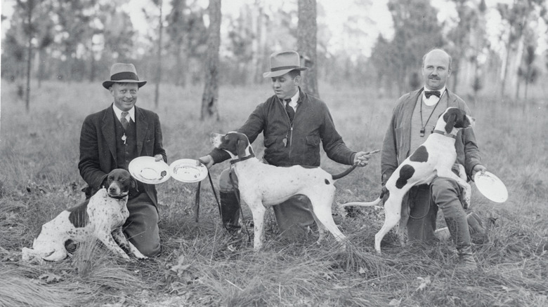 Three men pose with their hunter dogs in an early 1900s photo