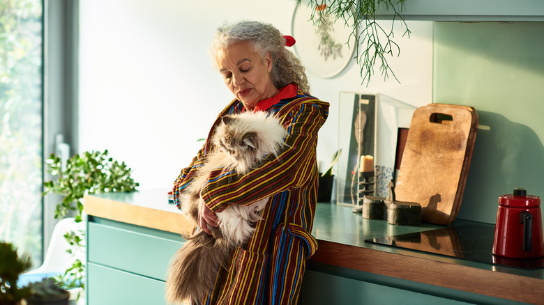 a mature woman stands alone in an apartment, holding a fluffy cat