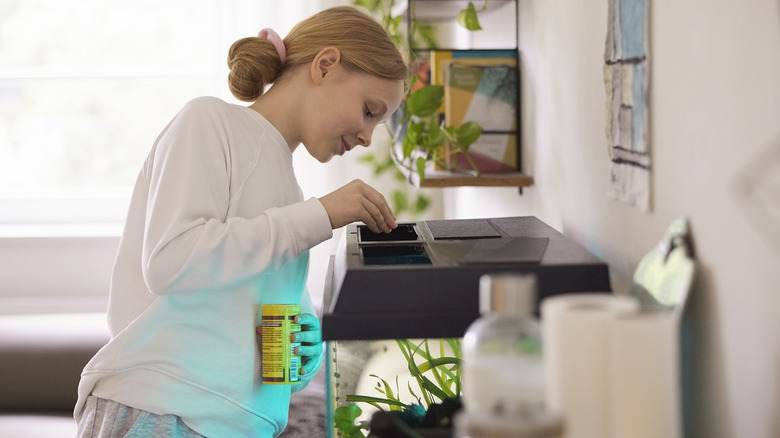 a teenage girl feeding fish in a home aquarium