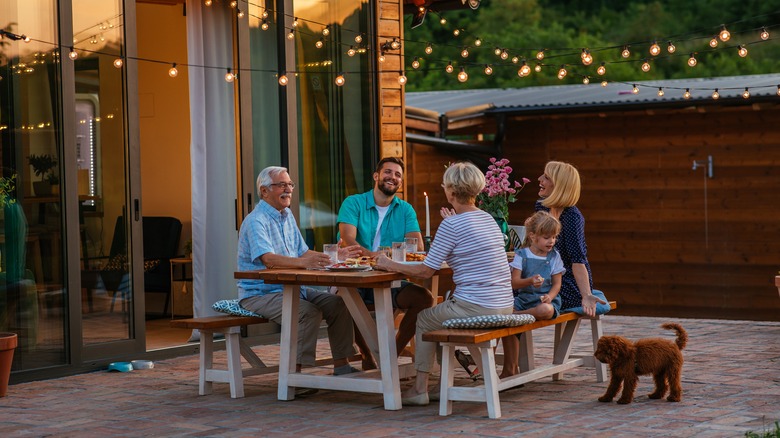 A happy family seated at an outdoor picnic table, laughing and eating, while a little girl looks at the family dog instead