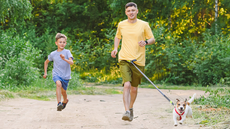 Man and child running with dog while dog's leash is attached to man's waist