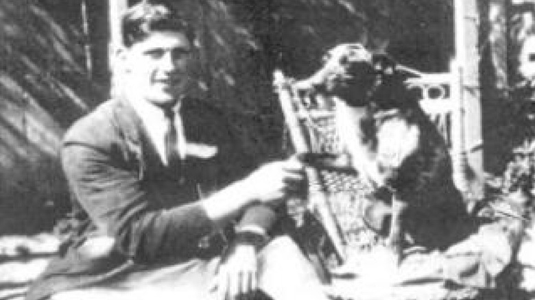 Man holding Bluey's paw while he's seated on a chair