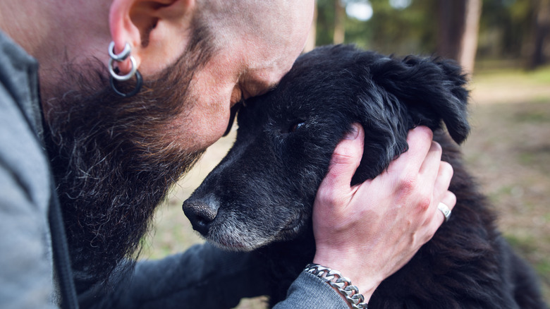 Man sadly places his head against his older black dog