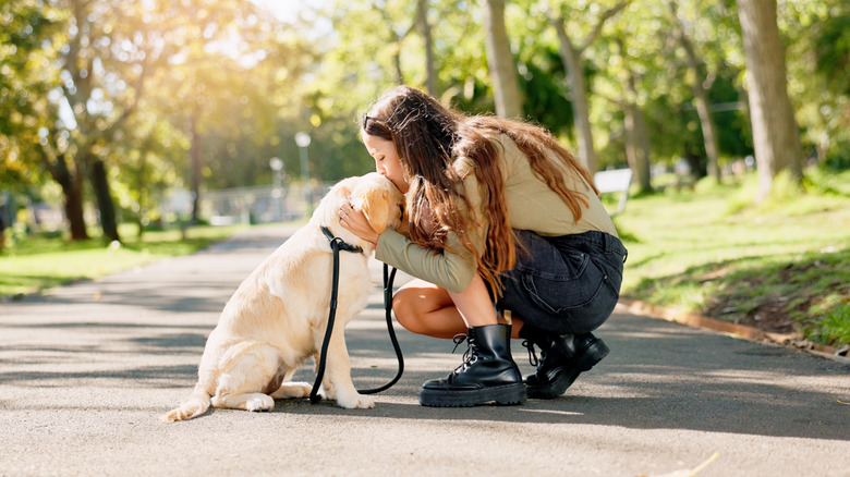 A woman in the park bends down to kiss her Labrador on the head