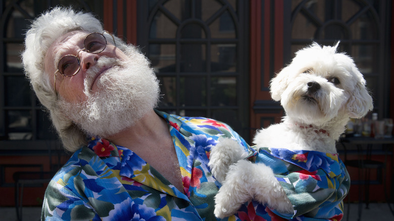 An old man poses with his dog dressed and looking the same as him