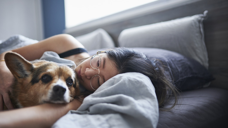 A woman rests in bed with a dog laying on her arm