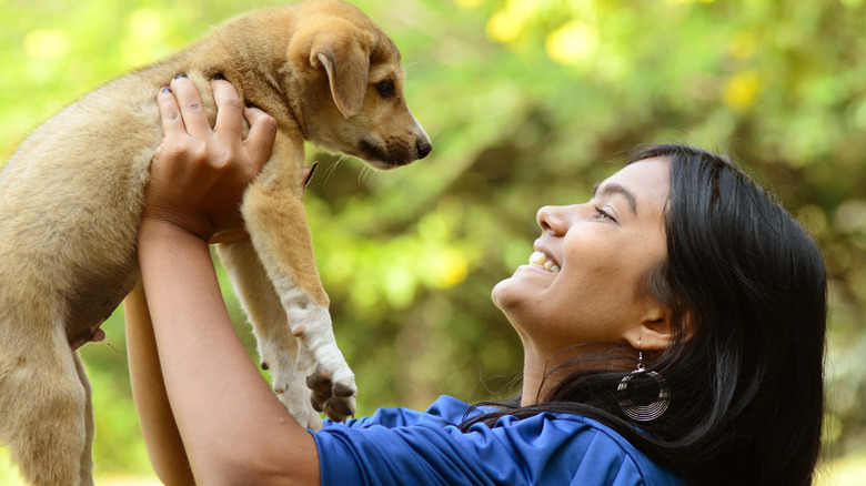 young woman holding a puppy up in front of her face and making eye contact