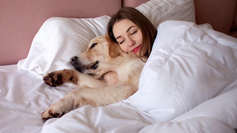 Woman sleeping with her dog in white bedding