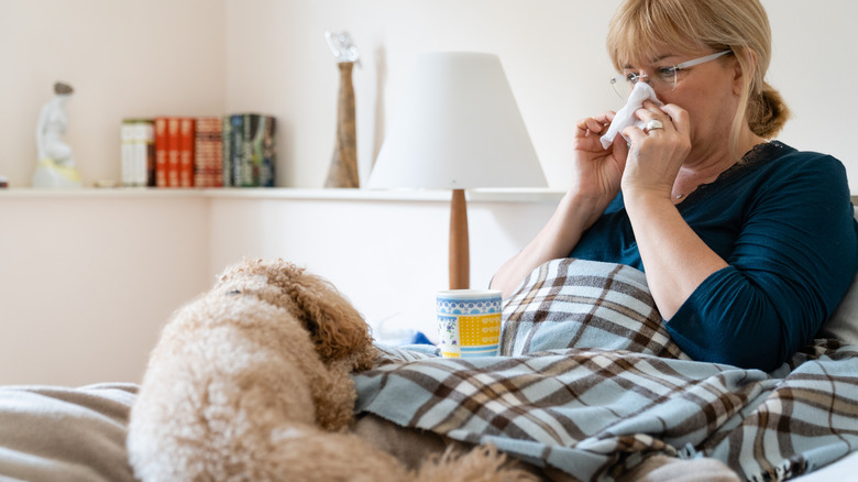 woman blowing her nose next to her dog