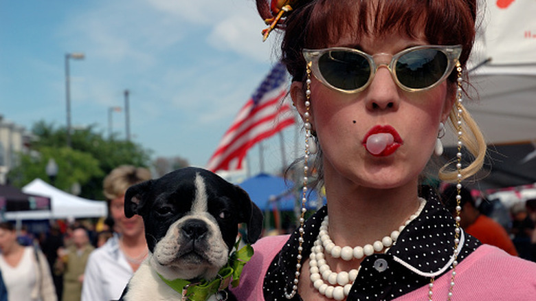 A woman blowing a bubble with gum while holding a dog