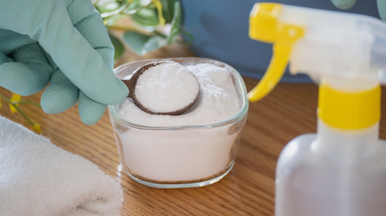 A gloved hand spoons baking soda out of a glass jar.