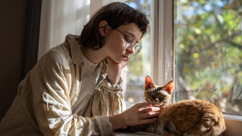 Sad woman petting cat on window perch