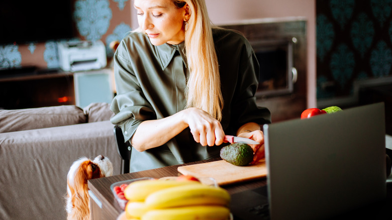 Woman slicing an avocado while a cavalier king Charles spaniel looks up from the floor